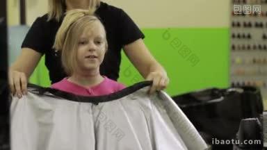 专业年轻的女理发师准备为可爱的女孩做发型，在美发与孩子交谈时披着睡衣